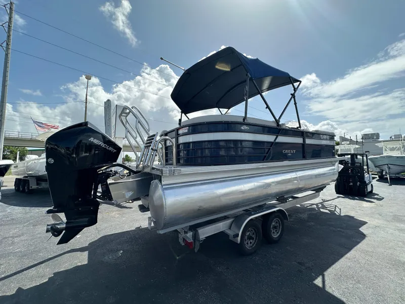 Slide: The Image of 2022 Crest Classic DLX 220 pontoon boat with canopy on trailer under sunny sky. - 2