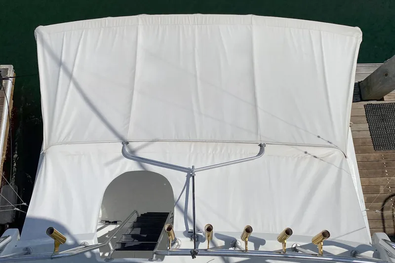 Slide: The Image of 1990 Hatteras 58 Sportfish boat with white canopy and fishing rod holders, docked at marina. - 12