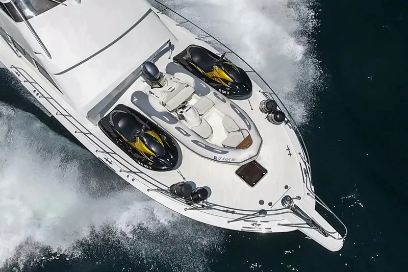 Slide: The Image of 1990 Hatteras 58 Sportfish yacht with jet skis on deck, cruising through water. - 2