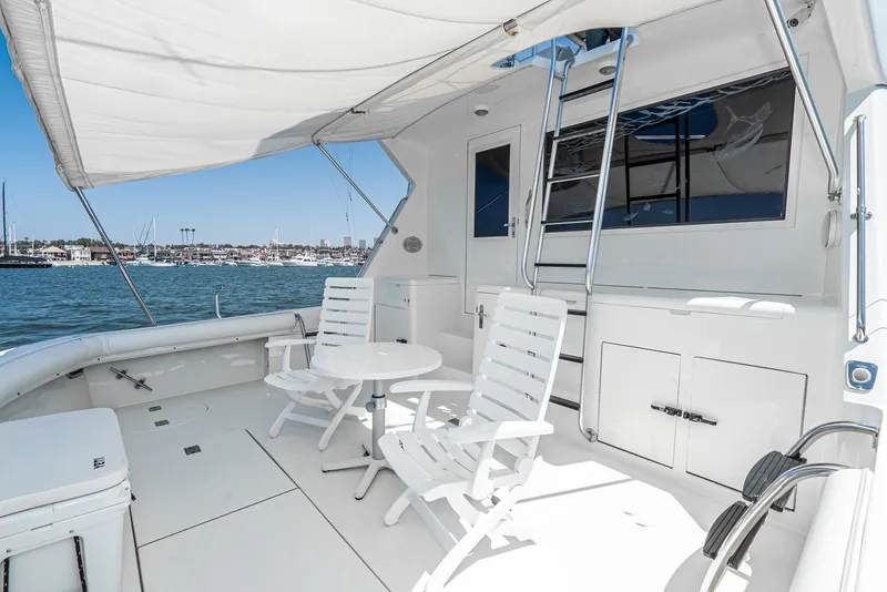 Slide: The Image of 1990 Hatteras 58 Sportfish yacht deck with white chairs and table, overlooking marina. - 21