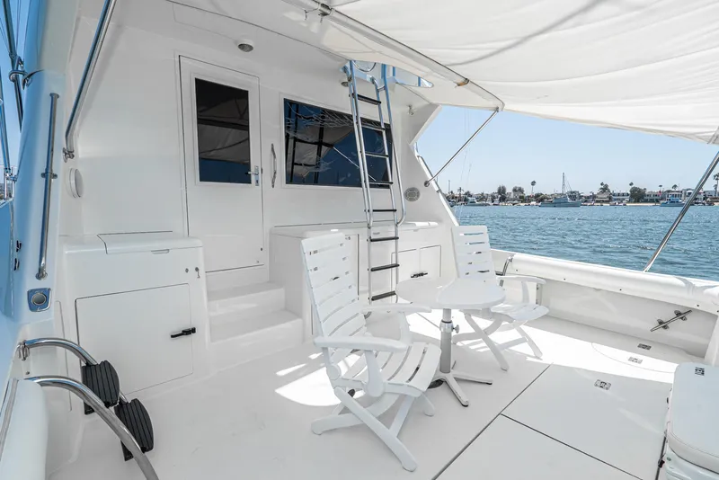 Slide: The Image of 1990 Hatteras 58 Sportfish yacht deck with white chairs and table, overlooking calm waters. - 22