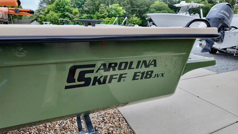Slide: The Image of 2025 Carolina Skiff E18 JVX Swamp Edition boat, green hull, parked outdoors. - 2