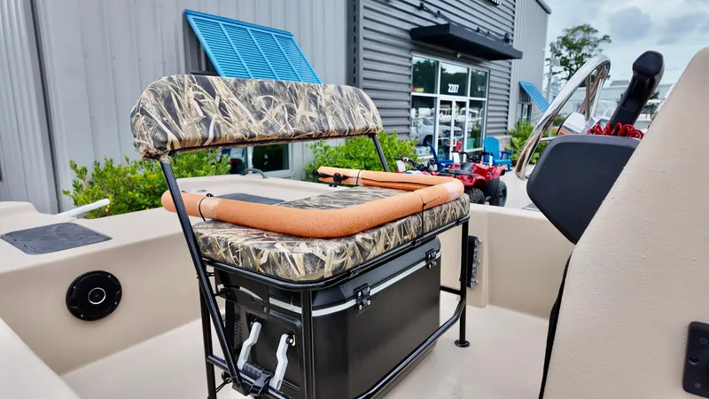 Slide: The Image of 2025 Carolina Skiff E18 JVX Swamp Edition boat with camo seating and storage, parked outside a building. - 6
