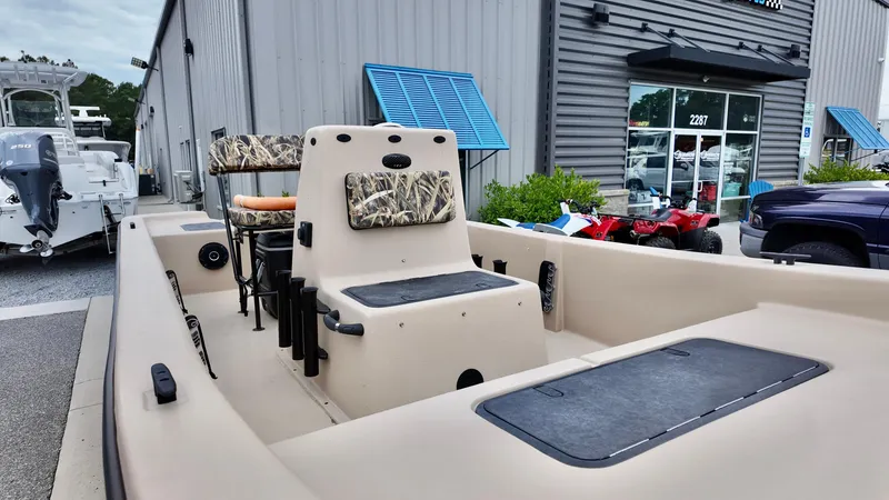 Slide: The Image of 2025 Carolina Skiff E18 JVX Swamp Edition boat with camo seats, parked outside a showroom. - 8