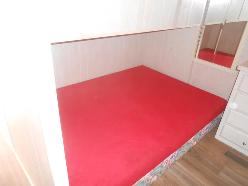 Slide: The Image of 1994 Stardust Cruisers houseboat bedroom with red bedspread, wood flooring, and mirrored closet. - 17