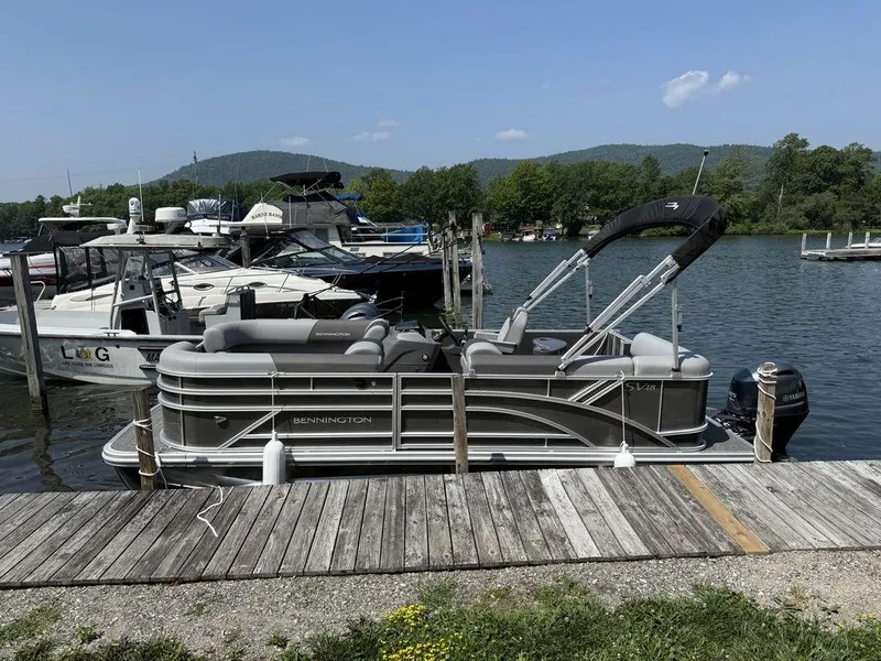The Image of 2025 Bennington S L-Bench 18SVL pontoon boat docked by a scenic lake. - 1