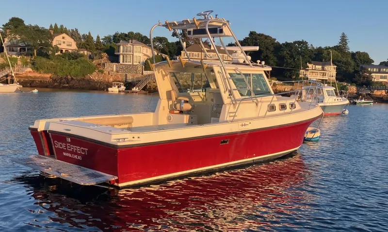 Slide: The Image of 1997 Albin 28 Tournament boat with red hull, docked in a scenic coastal area. - 5