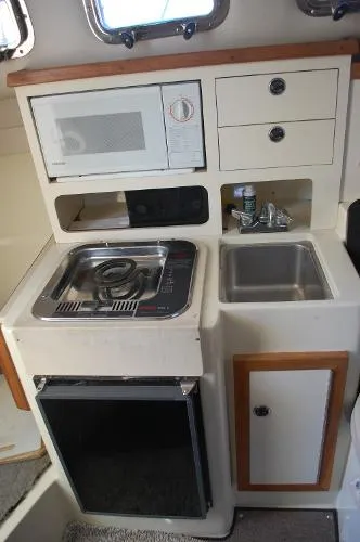 Slide: The Image of 1997 Albin 28 Tournament boat kitchenette with stove, sink, microwave, and storage cabinets. - 8