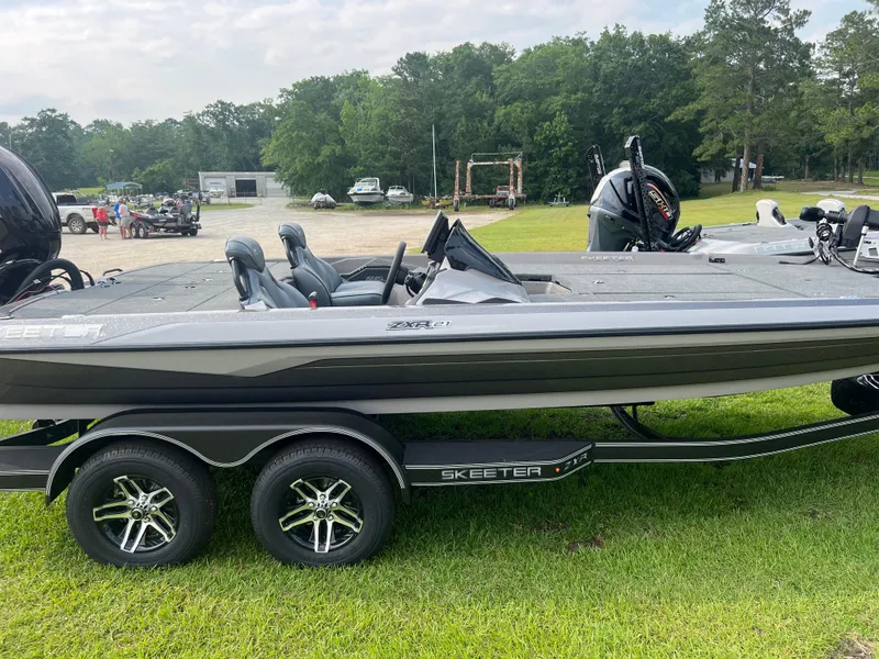Slide: The Image of 2025 Skeeter ZXR 21 boat on trailer, parked on grass with trees in background. - 7