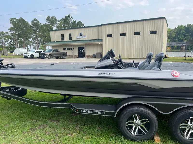 Slide: The Image of 2025 Skeeter ZXR 21 boat on trailer, parked outside a building with trees in the background. - 8
