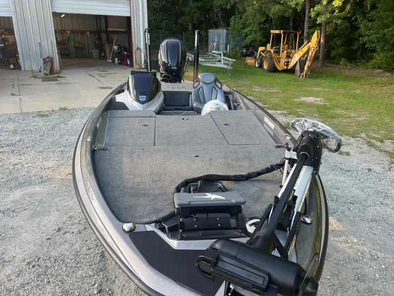 Slide: The Image of 2025 Skeeter ZXR 21 boat with motor, parked outdoors near a garage and construction equipment. - 9