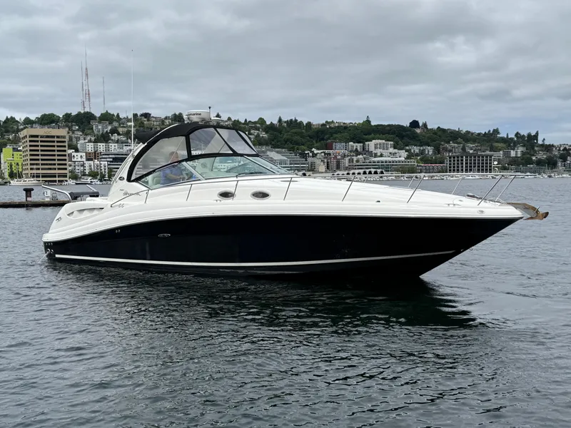 The Image of 2008 Sea Ray 340 Sundancer boat on calm water, overcast sky, urban backdrop. - 0
