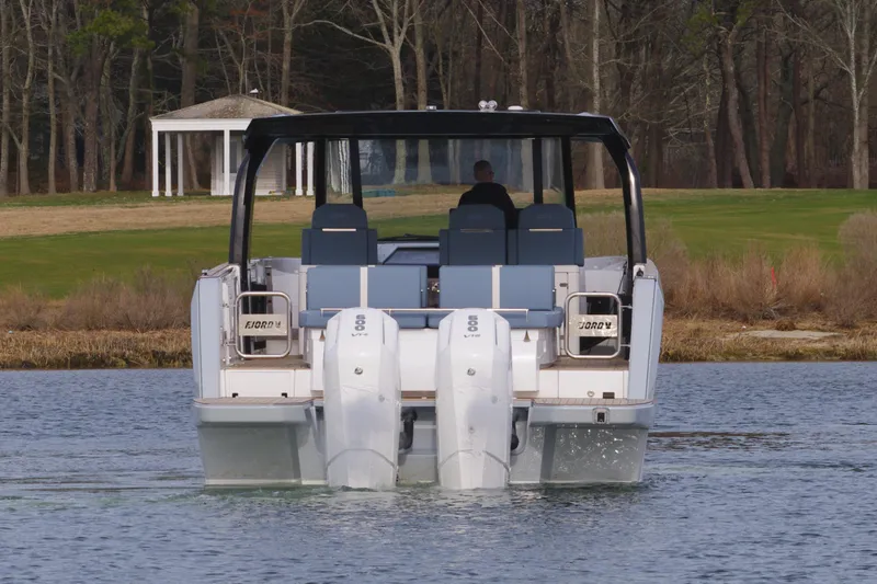 Slide: The Image of 2025 Fjord 41 XP boat on water, rear view with dual engines, surrounded by trees. - 6