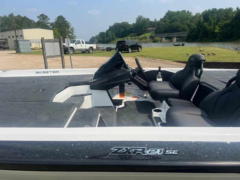 Slide: The Image of 2025 Skeeter ZXR 21 boat interior with seating and steering, parked near a lake. - 2