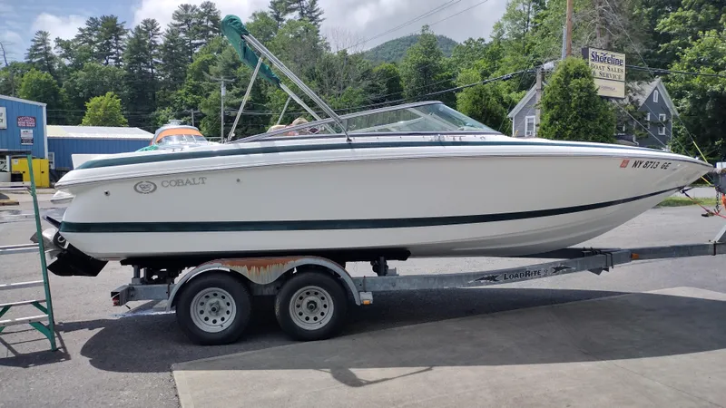 Slide: The Image of 1999 Cobalt 226 boat on trailer, parked outdoors with trees in background. - 3