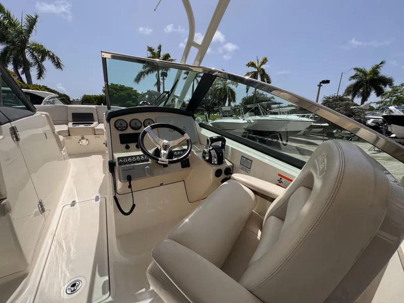Slide: The Image of 2014 Boston Whaler 270 Vantage boat cockpit with steering wheel and controls, palm trees in background. - 11