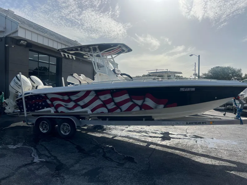 Slide: The Image of 2019 Glasstream 280 Pro-XS boat with American flag design on trailer, parked outdoors. - 1
