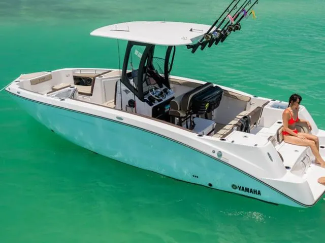 Slide: The Image of 2025 Yamaha Boats 255 FSH Sport H in turquoise water with a person relaxing onboard. - 23