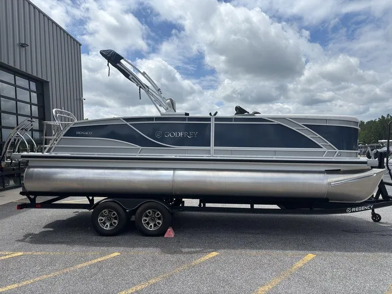 The Image of 2025 Godfrey Monaco 235 SFL pontoon boat on trailer, parked outdoors. - 1