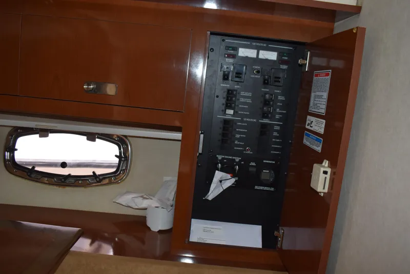 Slide: The Image of Electrical panel inside 2011 Sea Ray 310 Sundancer boat cabin, with wooden cabinetry and porthole. - 39