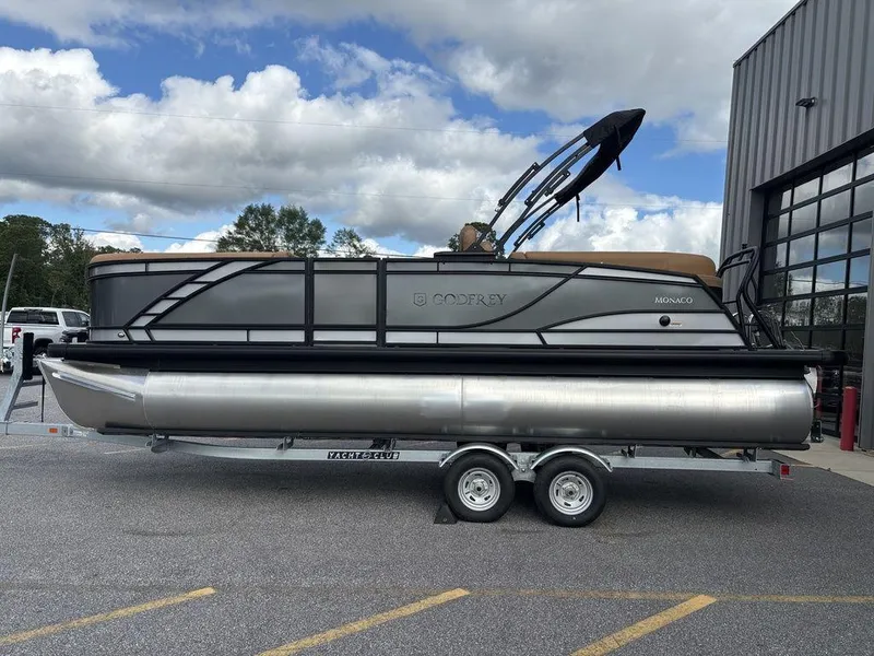 The Image of 2025 Godfrey Monaco 235 SB pontoon boat on trailer, parked outdoors. - 1