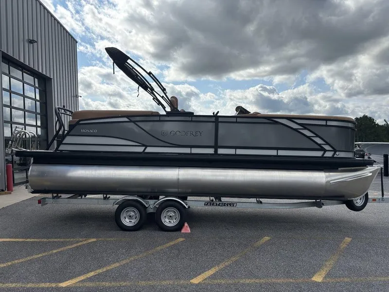 Slide: The Image of 2025 Godfrey Monaco 235 SB pontoon boat on trailer, parked outdoors under cloudy sky. - 6