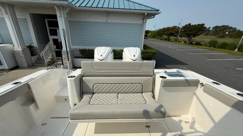 Slide: The Image of 2025 Pursuit S 328 Sport boat with cushioned seating and dual engines, docked near a building. - 12