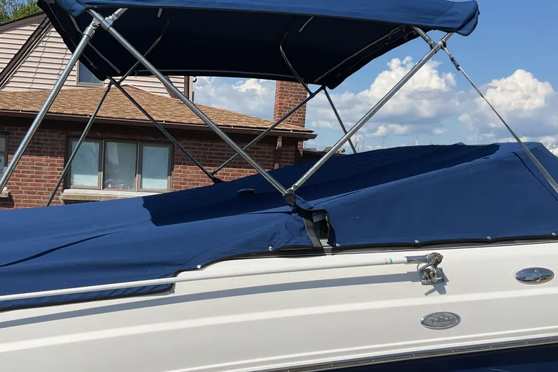 Slide: The Image of 2006 Chaparral 256 SSi boat with blue canopy and cover, parked near a brick building. - 8