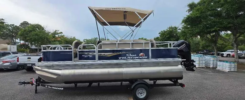 Slide: The Image of 2025 Sun Tracker Bass Buggy 18 DLX pontoon boat on trailer in parking lot. - 2