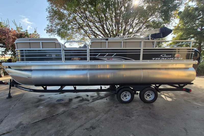 The Image of 2023 Sun Tracker SportFish 22 XP3 pontoon boat on trailer, parked outdoors. - 0