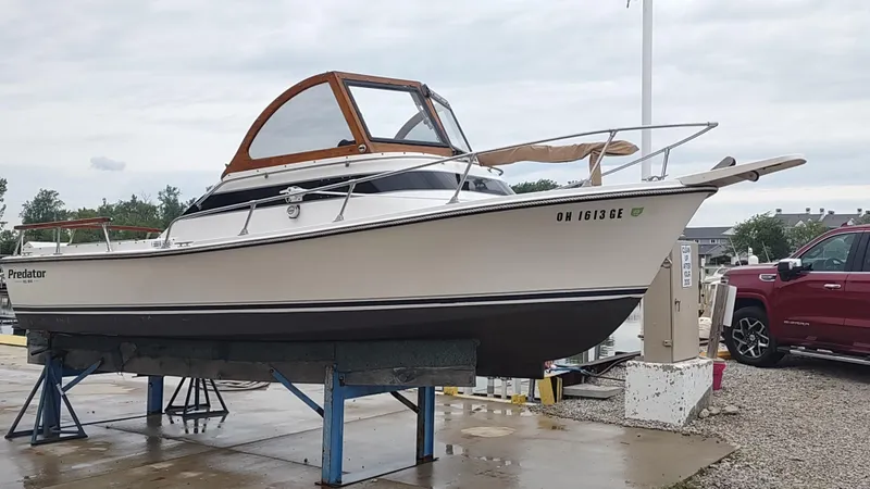 The Image of 1988 Shamrock 220 Predator boat on stands, white hull, wooden cabin, overcast sky. - 1