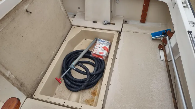 Slide: The Image of 1988 Shamrock 220 Predator boat interior with storage compartment, hose, and cleaning supplies. - 10