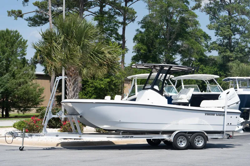 Slide: The Image of 2026 Twin Vee 22 Baycat boat on trailer, parked outdoors with trees in the background. - 12