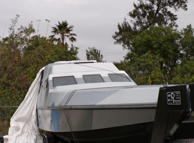 Slide: The Image of Custom Revenge 50 boat from 2001, partially covered, surrounded by trees and foliage. - 25