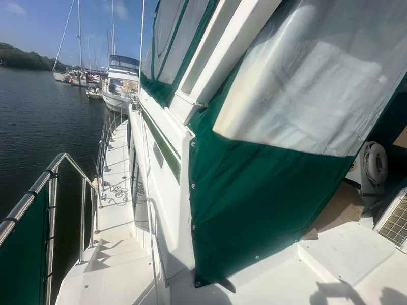 Slide: The Image of 1989 Bluewater 51' Coastal Cruiser docked, featuring green canvas covers and a spacious deck. - 11