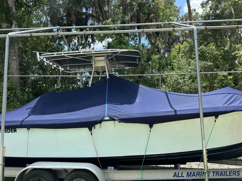 Slide: The Image of 1985 Contender 25 Classic boat on trailer, covered with blue tarp, surrounded by trees. - 3