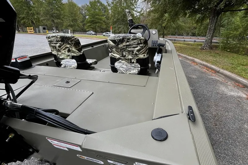 Slide: The Image of 2025 Tracker Grizzly 1754 SC boat with camo seats, parked near trees. - 16