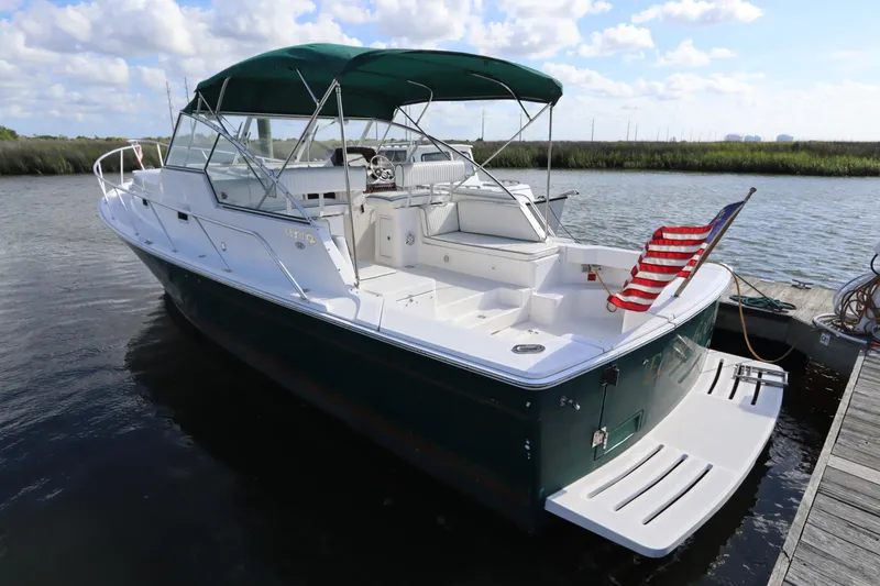 Slide: The Image of 2002 Mainship Pilot 34 boat docked, featuring green hull and American flag chair. - 2