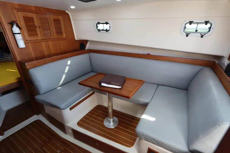 Slide: The Image of 2002 Mainship Pilot 34 interior with gray seating, wooden table, and porthole windows. - 42