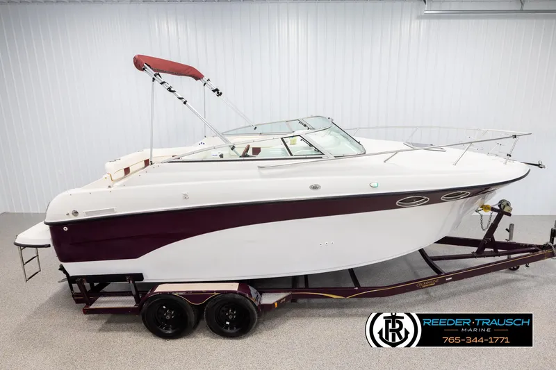 The Image of 1999 Crownline 242 CR boat on trailer, white and maroon, with canopy, in showroom. - 1