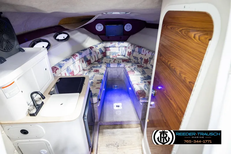 Slide: The Image of 1999 Crownline 242 CR cabin interior with kitchenette, seating, and wood accents. - 32