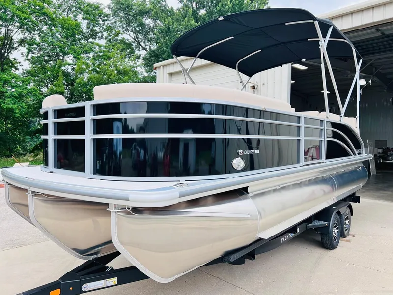 Slide: The Image of 2025 Harris Cruiser 230 pontoon boat with black canopy, parked on a trailer. - 2
