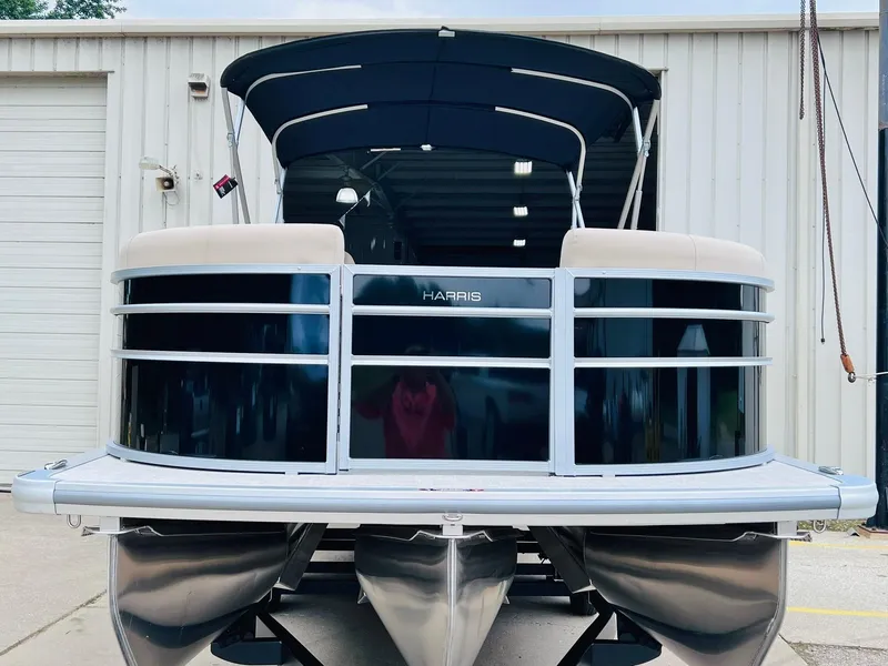 Slide: The Image of 2025 Harris Cruiser 230 pontoon boat, front view, parked outside a warehouse. - 4