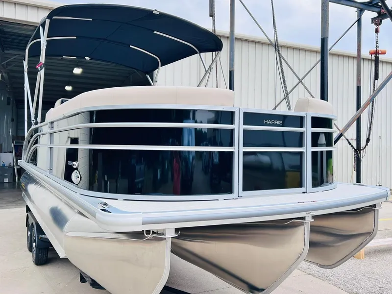 Slide: The Image of 2025 Harris Cruiser 230 pontoon boat with canopy, docked near a warehouse. - 5