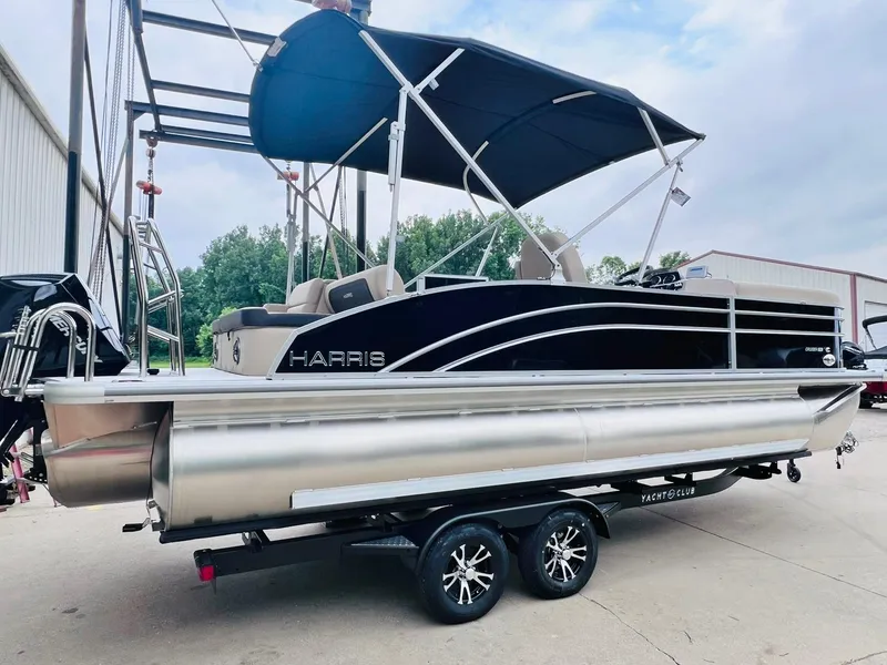 Slide: The Image of 2025 Harris Cruiser 230 pontoon boat on trailer with canopy, parked outdoors. - 6