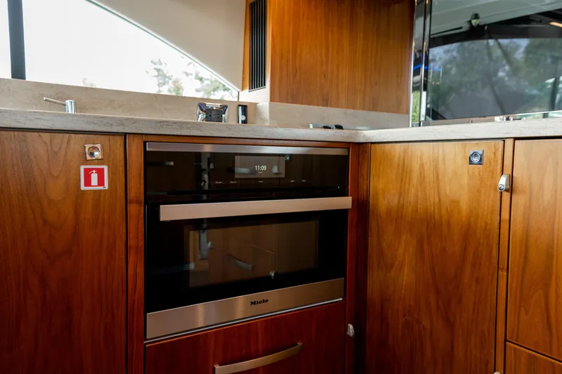Slide: The Image of Interior of 2018 Riviera 5400 Sport Yacht kitchen with wooden cabinetry and modern appliances. - 12