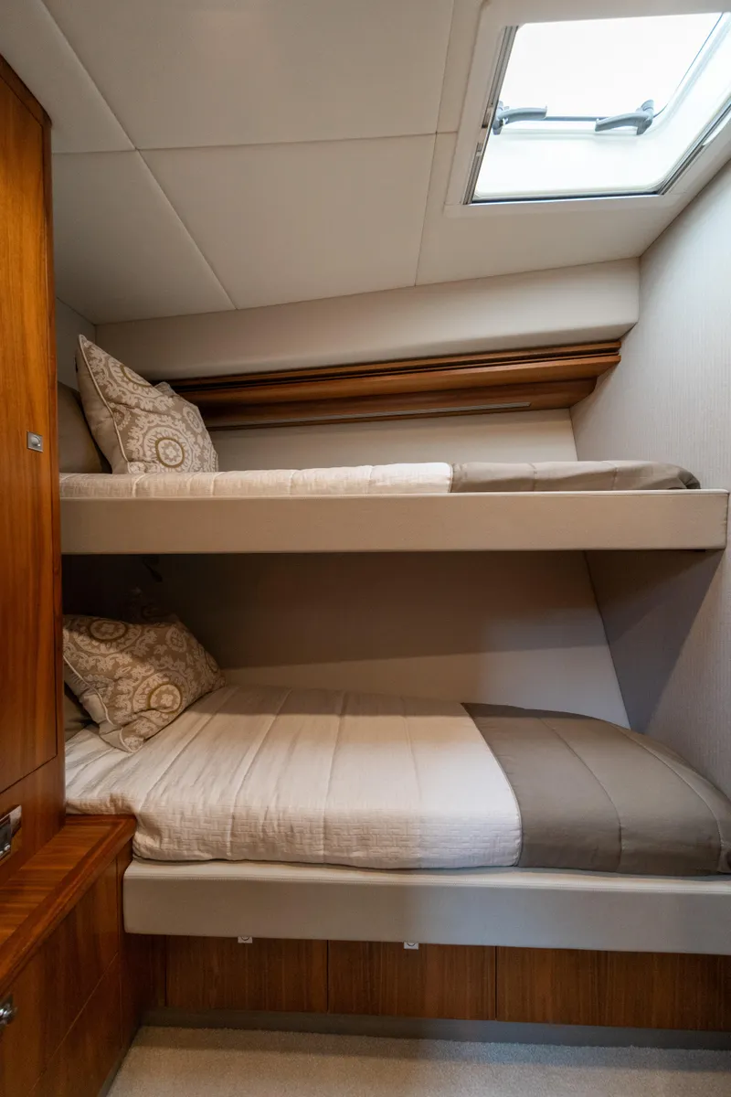 Slide: The Image of 2018 Riviera 5400 Sport Yacht cabin with bunk beds and natural light. - 19