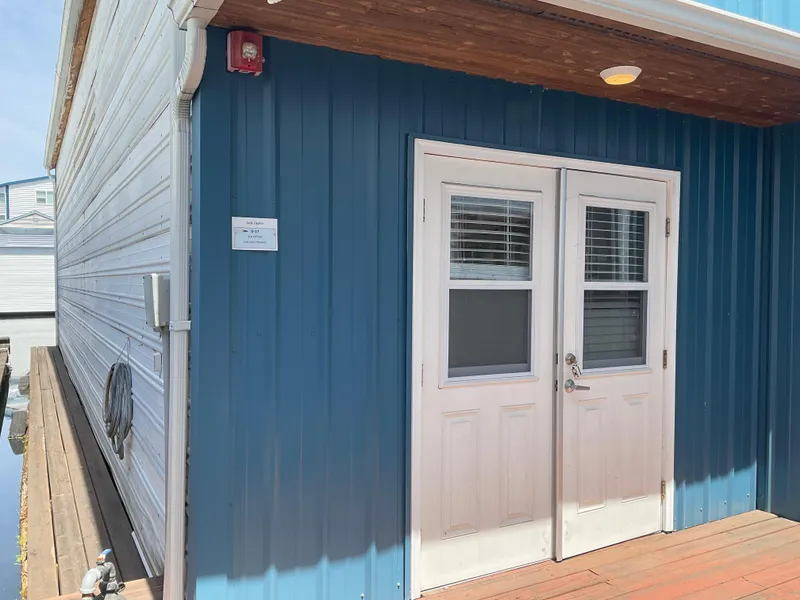 Slide: The Image of Custom 1980 boathouse with blue siding and white double doors on a wooden deck. - 3