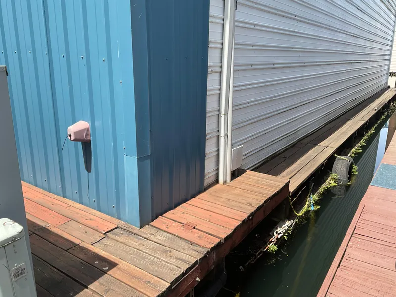 Slide: The Image of Wooden walkway beside a custom 1980 boathouse with blue and white siding. - 4