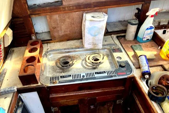 Slide: The Image of 1977 Catalina 30 Tall Rig kitchen with stove, cleaning supplies, and wooden storage. - 8